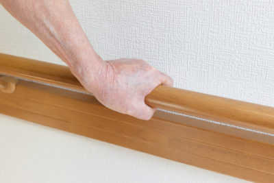 An older adult hand holds on to a wooden banister for support