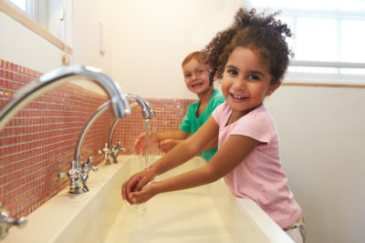 Two children washing hands in sink and smiling at the camera