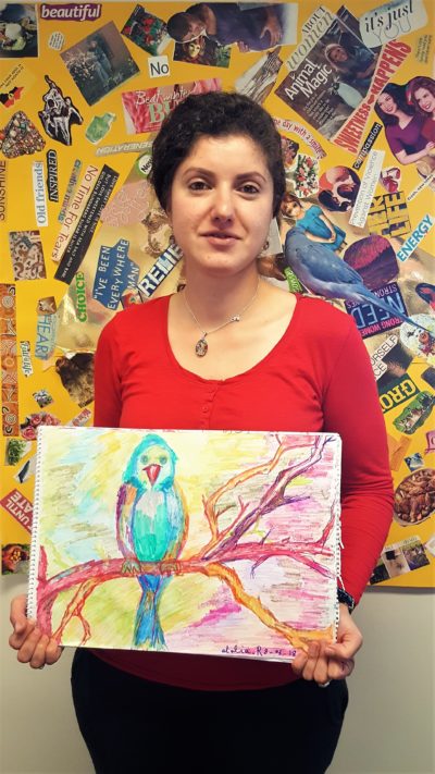 Atalia holds up one of her paintings of a parrot