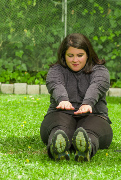A woman sits on the grass stretching towards her toes