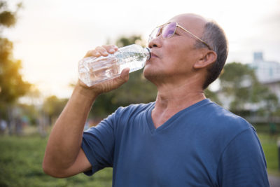 Older man drinks form water bottle outside