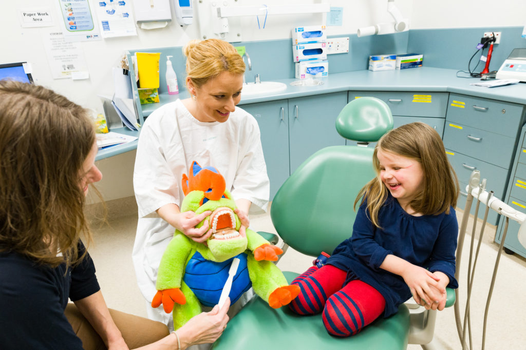 Dental assistant shows child and parent how to brush teeth with Dino the Dental Dinosaur