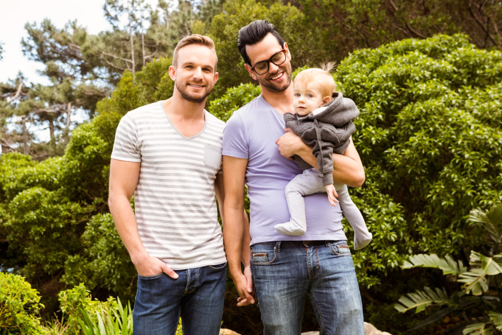 Two dads with young baby with garden in background