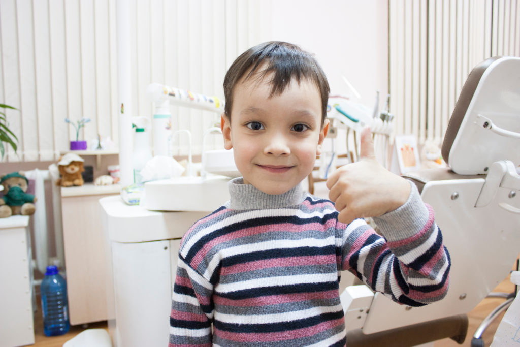 Young child in dental surgery gives thumbs up