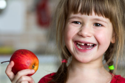 Girl with missing tooth holds an apple