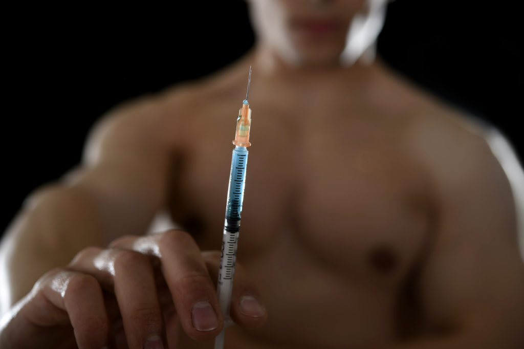 Close up of steroid injection needle held by man who is blurred out in the background