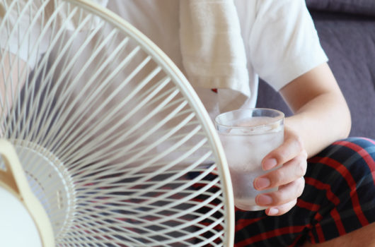 Glass of water and cool towel in from of fan. Hot day concept.