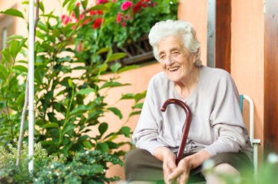 Older woman sitting on her front porch holding walking stick