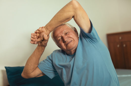 Older man stretches arms over head whilst seated