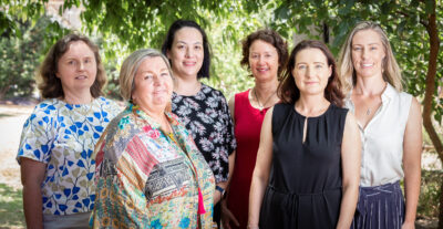 Five women facing camera smiling, in a garden