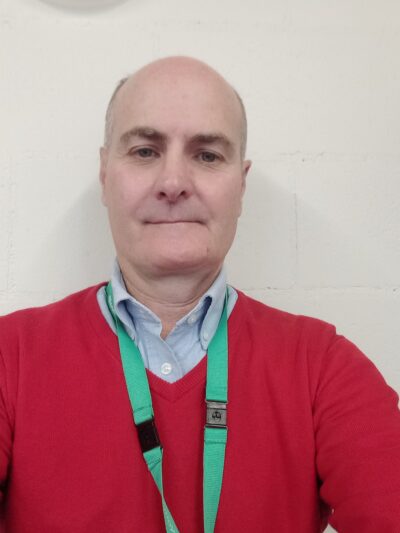 Head shot of white man in a red jumper wearing a green lanyard.